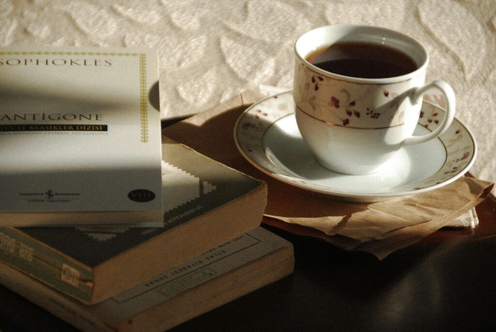 A still life featuring a floral tea cup on saucer beside a stack of classic books in warm light.